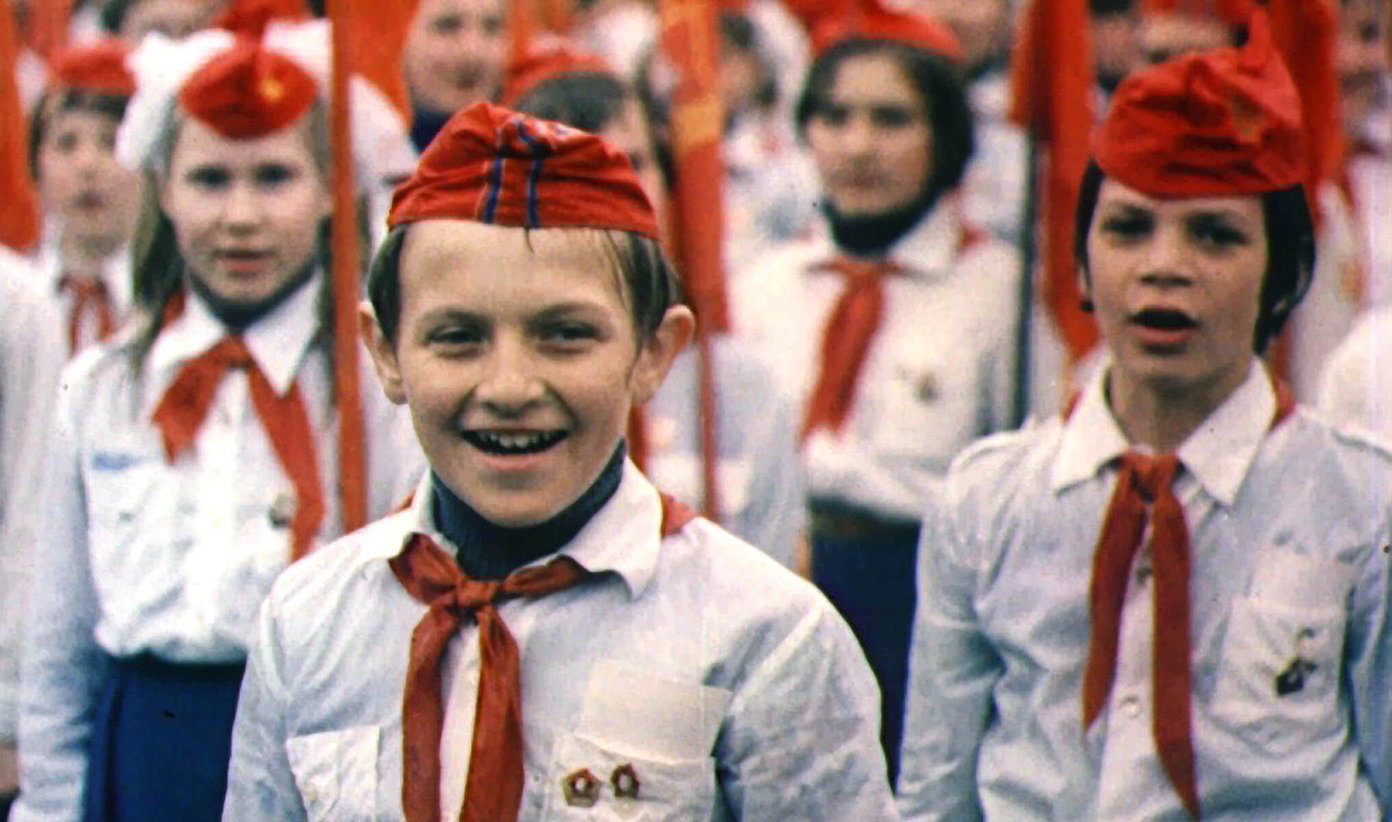 Still from My Perestroika. Rows of children wearing uniforms of white button down shirts, red ties, and red hats.