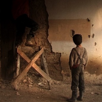 Still from Our School. A young boy stands looking at a man working on the foundation of a building.