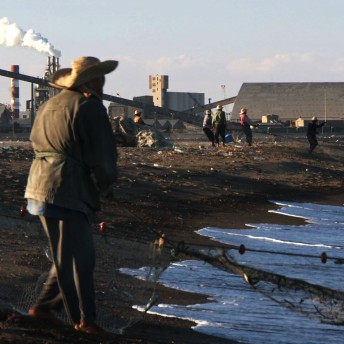 A still from The Factory and Me. A person in a dirt field walks towards a large puddle of water.