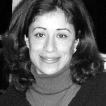 Sarra Abidi looks directly at the camera, smiling. Headshot in black and white.