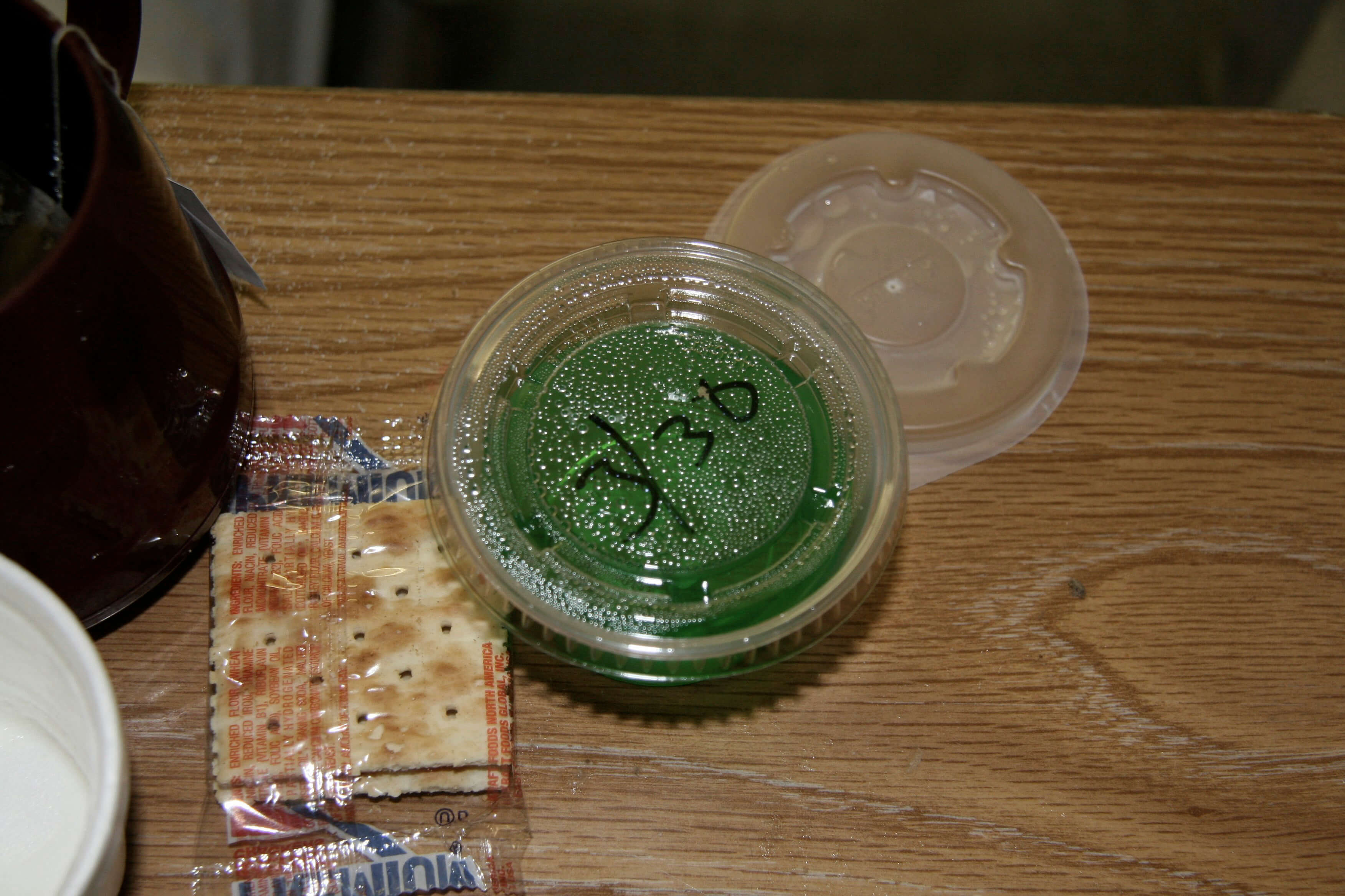 Still from The Patron Saints. A close-up shot of a packet of saltines and green sauce in a plastic ramekin atop a table. The top of the ramekin has "3/30" written on it in black marker.