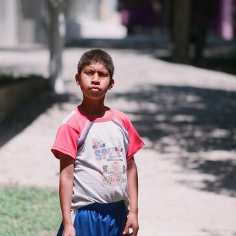 Still from Visitor's Day. A young boy stands outside looking at the camera inquisitively.