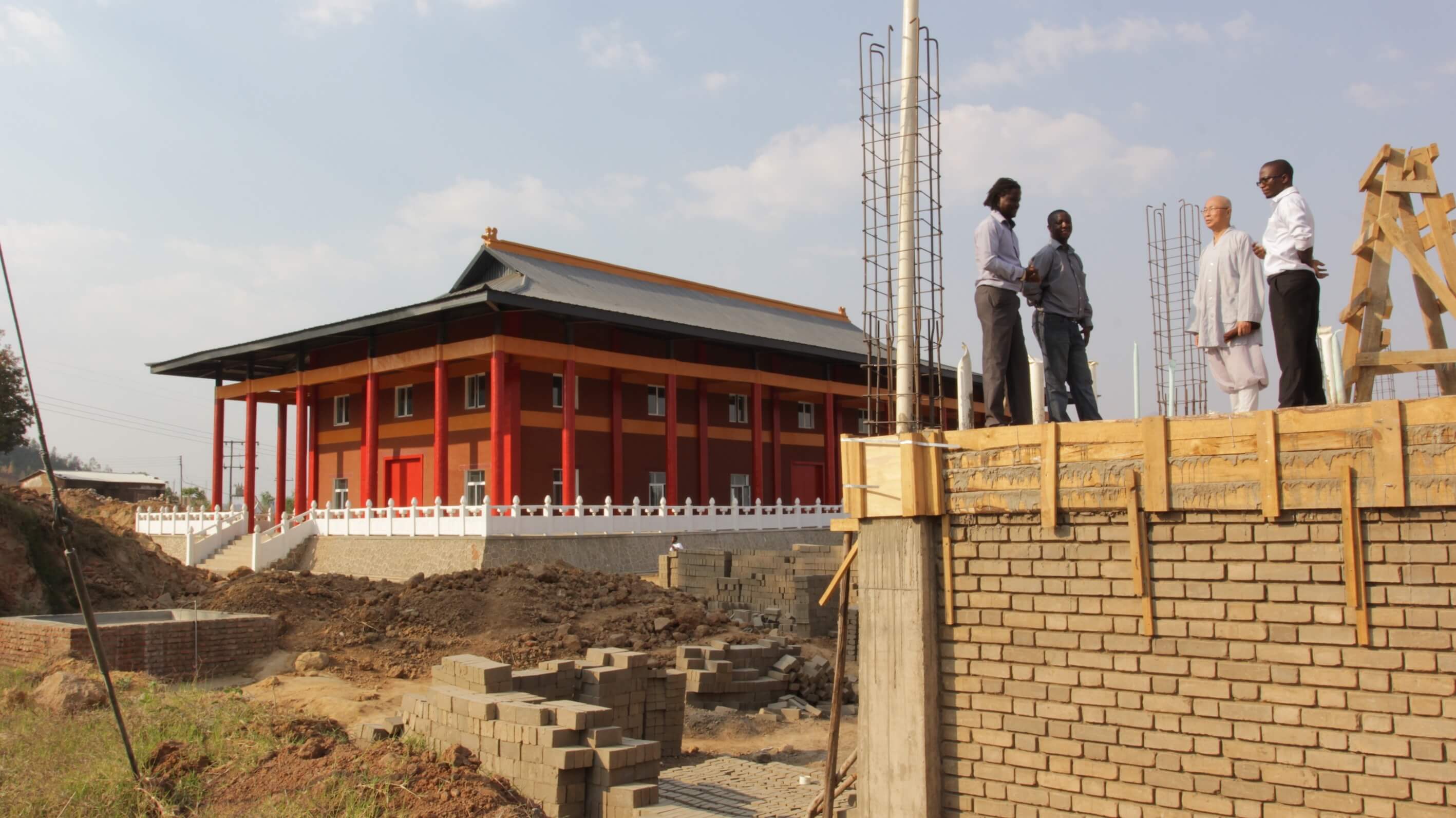 Two men are standing on the top of a construction building. In the background there are is a red Buddhist temple.