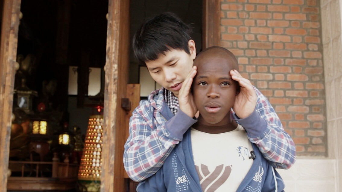 A man is standing behind a young man and uncovering his eyes.
