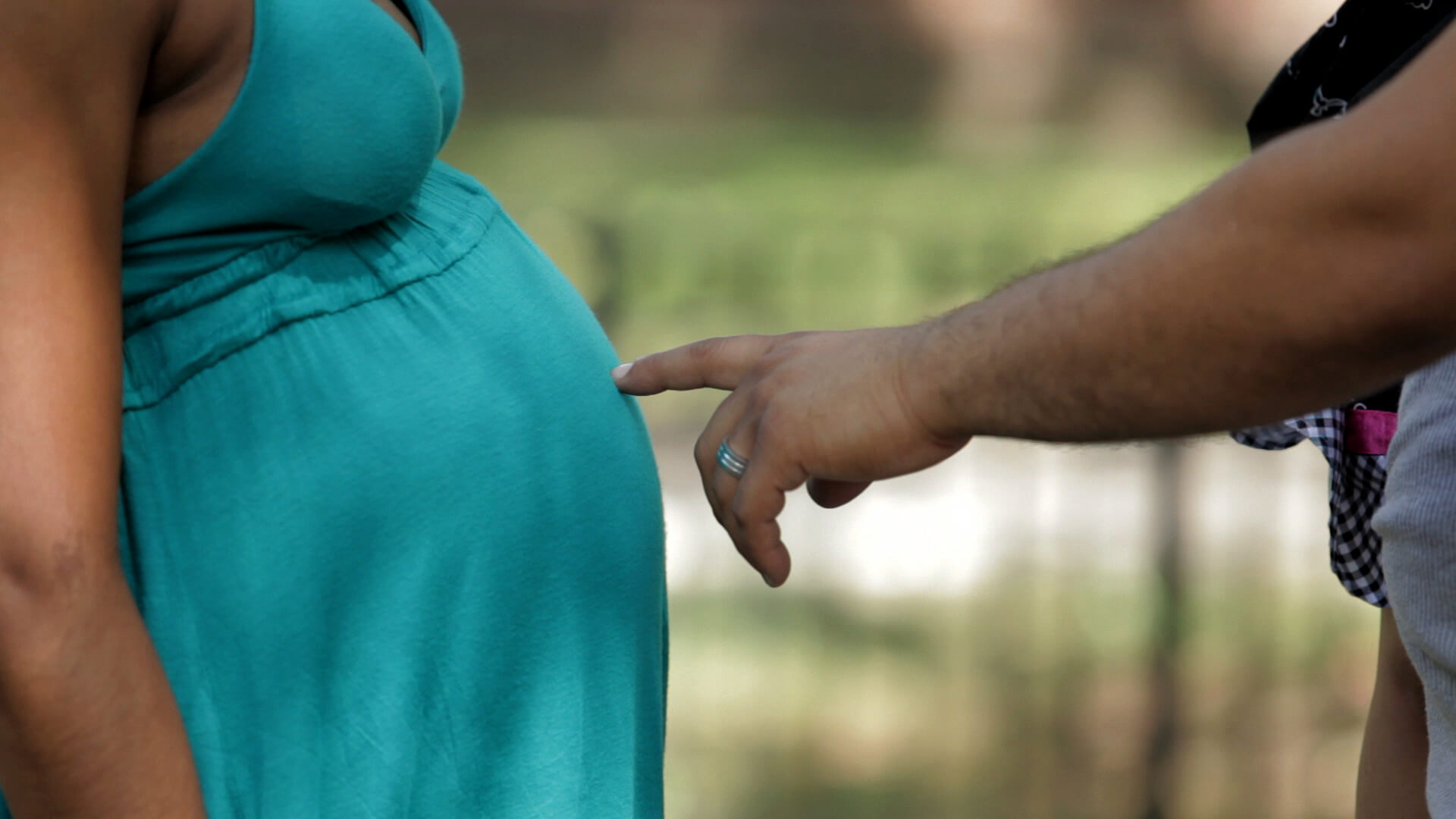 Still from Tough Love. Close-up of a hand pointing at a pregnant belly.