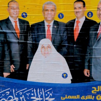 Still from The Vote. Photograph of a poster pasted on a wall. Three persons in suites are behind a person wearing a hijab.