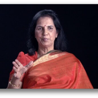 Suniti Solomon speaking to the camera in an orange Indian Sari.