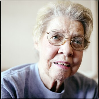 A still from The Graying of AIDS. A close-up shot of an older woman with short blonde hair and glasses.