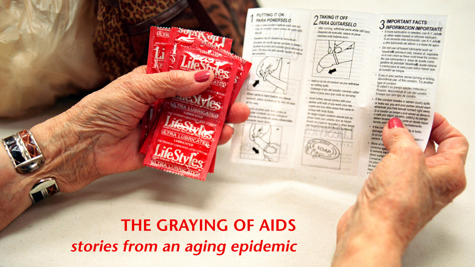 A graphic from The Graying of AIDS. A photo of a person's hands holding a bunch of condoms and a set of instructions for how to put on a condom. Their nails are painted red. There is red text on the bottom of the image that reads, "THE GRAYING OF AIDS stories from an aging epidemic".