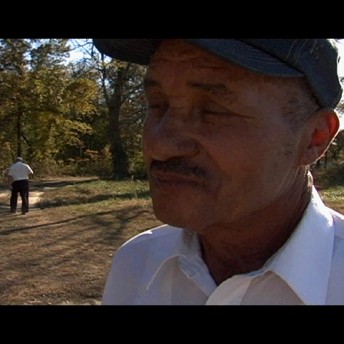 A still from The Color of Land. A close-up shot of a man in a blue hat and white shorts standing in a field with his eyes closed.
