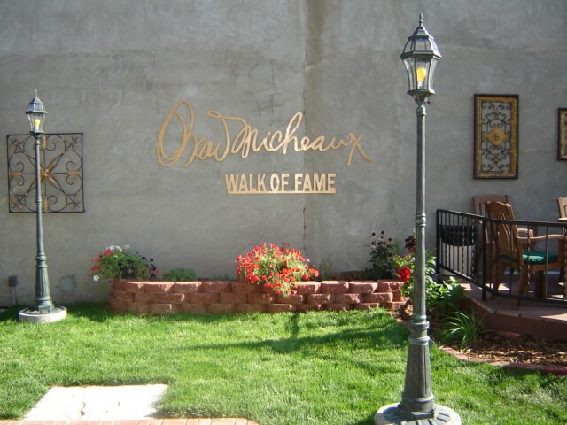 Still from Oscar's Comeback. In a courtyard area, the signature of Oscar Micheaux and words "Wall of Fame" are in a rose gold lettering on a cement wall. There are lamp posts and chairs around as well.