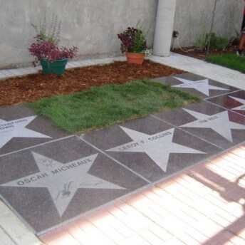 Still from Oscar's Comeback. In an outside area, there are 6 paved stars in the ground with names on each star.