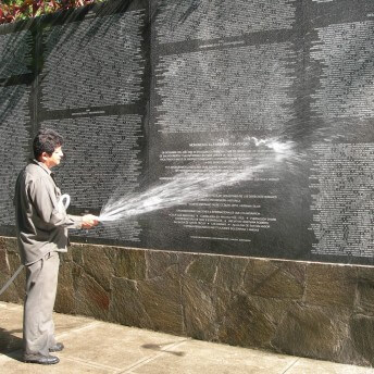A man cleaning with a water hose a wall with the names of the missing children of the civil war in El Salvador.