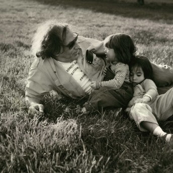 William Kunstler lies in the grass with his two young daughters Sarah and Emily Kuntsler. Black and white photograph.