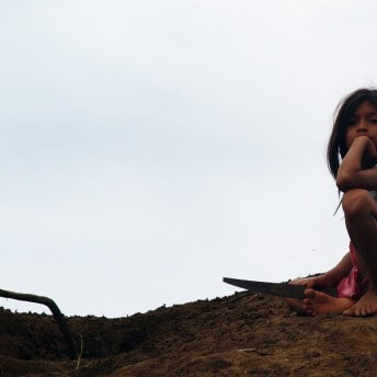 A young kid sits down in the soil holding a sharp object. Color photograph.
