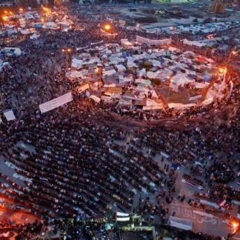 Diagonal overhead view of a large crowd surrounding a circle of tents at night.