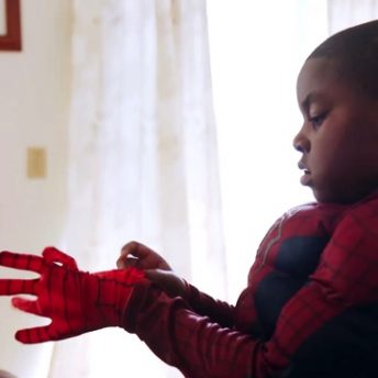 Still from Tre Maison Dasan. A young boy in a Spiderman suit is putting on a glove, part of his suit.
