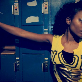 Still from United Skates. A woman in a yellow cut-off tank top stands in front of blue lockers. Her right arm is resting on the door of an open locker.