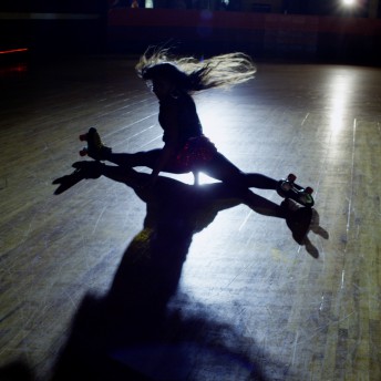 Still from United Skates. A woman in skates on a skating rink is doing the splits. The image is backlit.