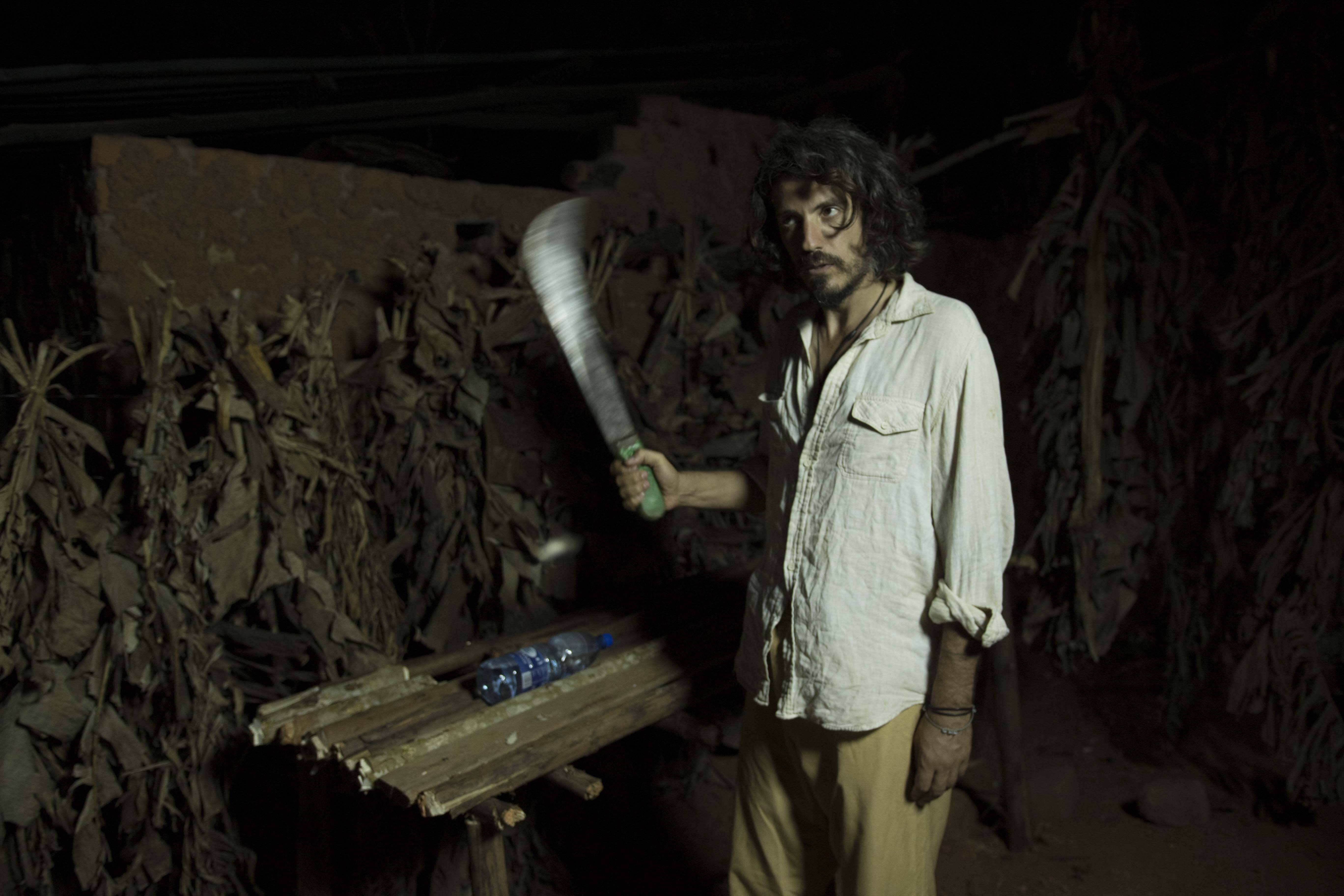 Still from Once Upon a Time in Uganda. A man stands in the dark, outside, near a table with a machete.
