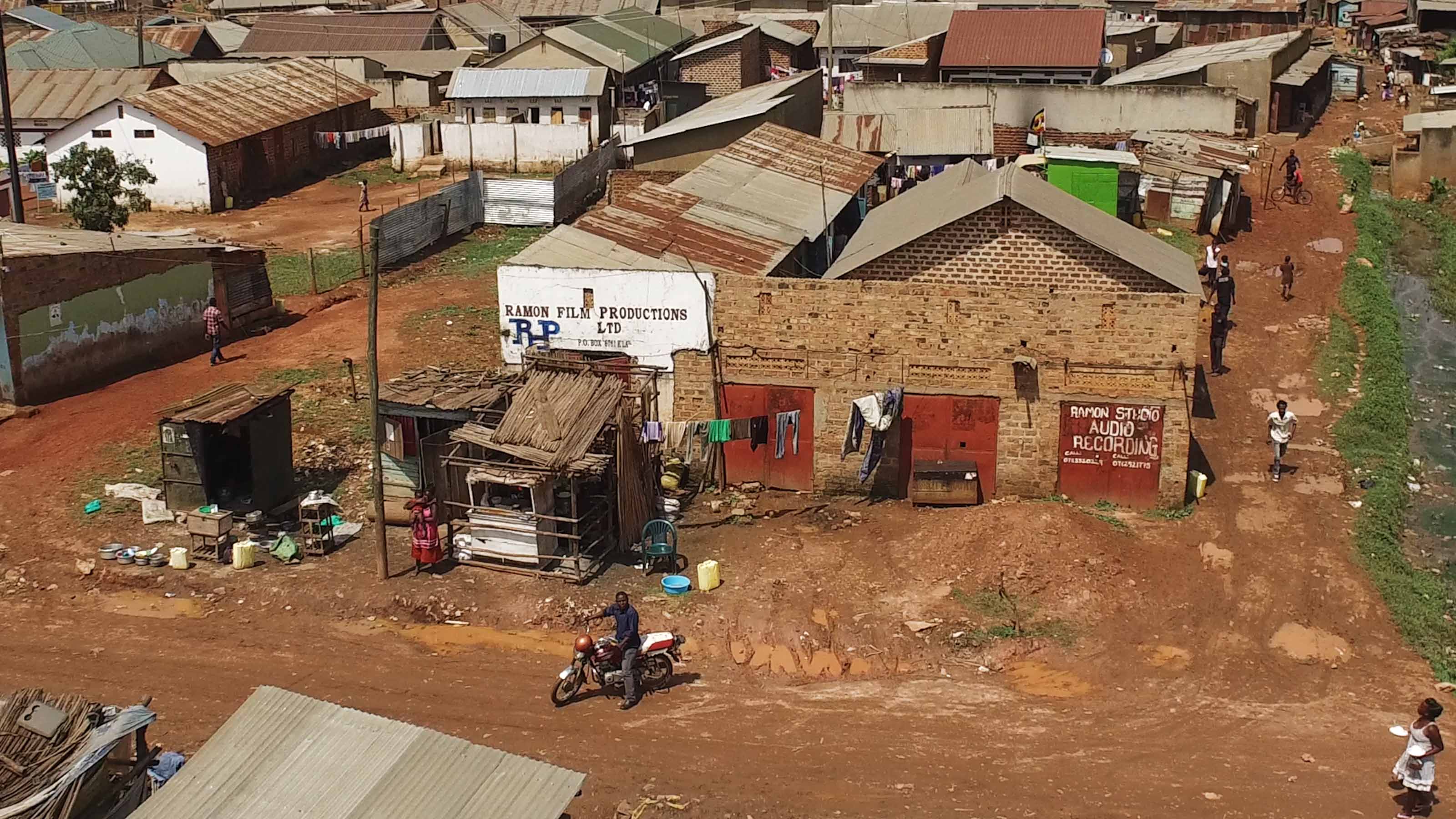 Still from Once Upon a Time in Uganda. An slight bird's eye view of a small village. There are people walking and on bikes.