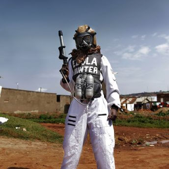 Still from Once Upon a Time in Uganda. A person standing outside with an "Ebola Hunter" hazmat suit on with a chemical sprayer.