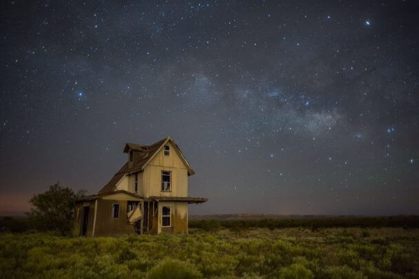 A still from The Guardian of Memory. A house sits off to the side on a grassy plain. It is night time and the sky is filled with stars and hues of blues and purples.