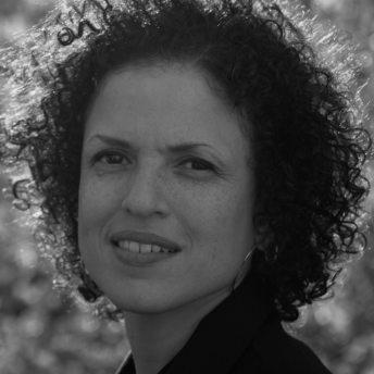 Michèle Stephenson looks at the camera, has curly short hair, and wears hoop earrings. Black and white portrait, trees out of focus in the background.