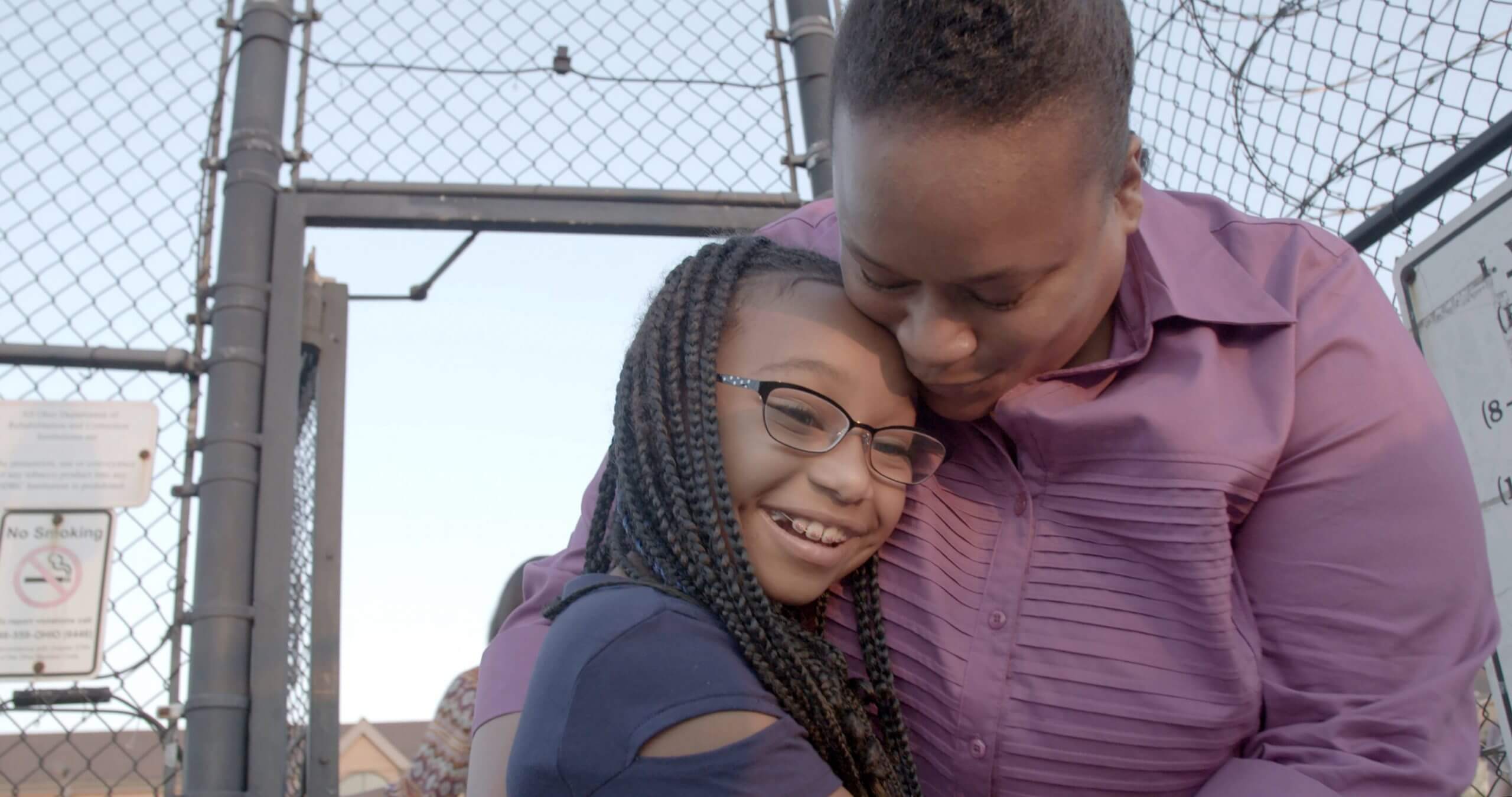 Still from Apart. Tomika and her daughter reunited. They are hugging outside of prison.
