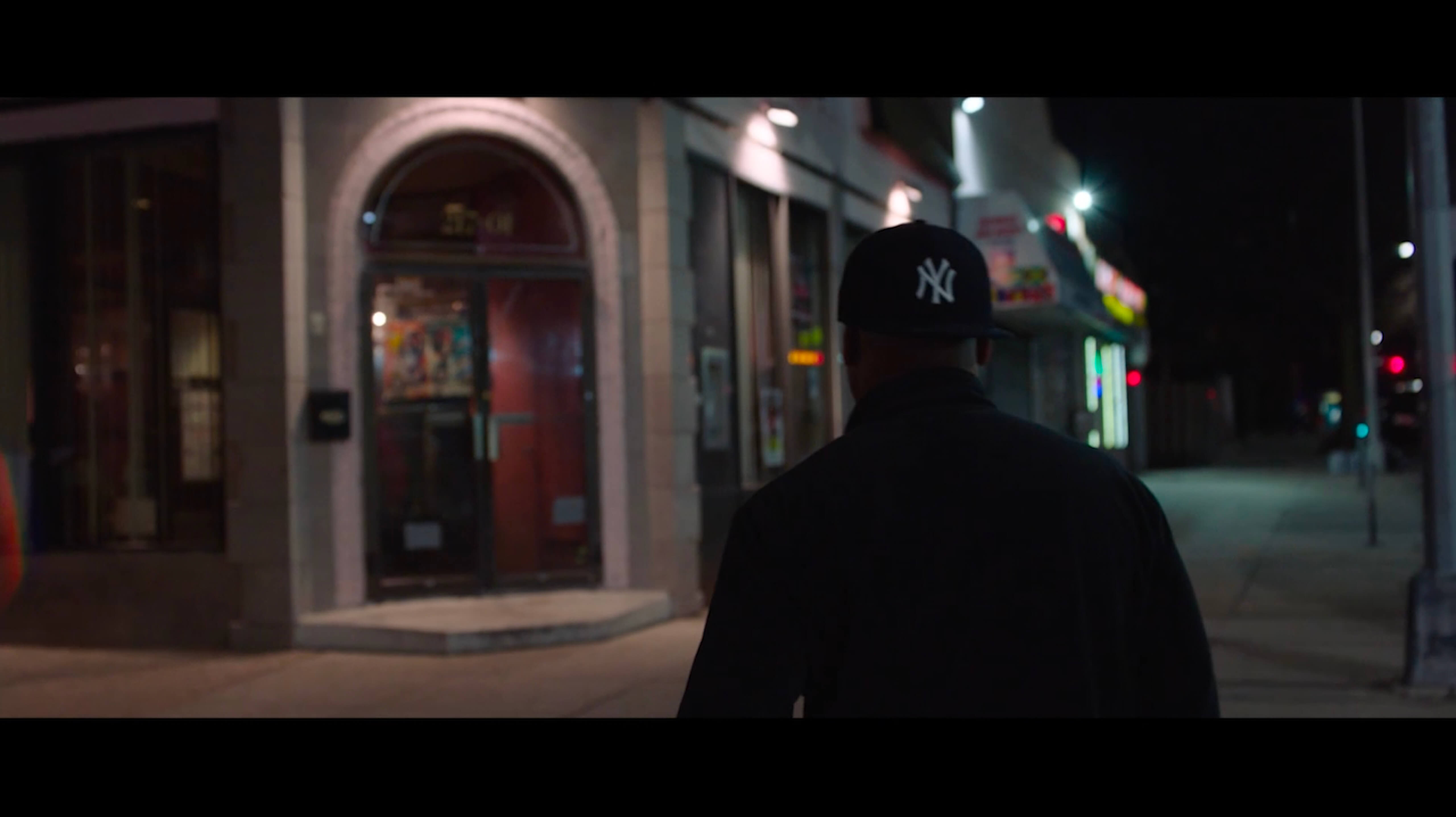 A man walking away from the camera wearing a Yankees cap.