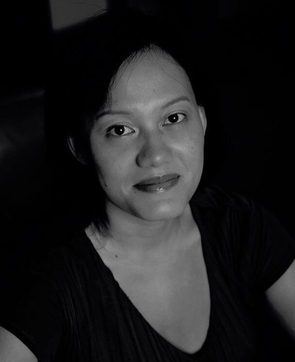Eunice Lau in black & white. Eunice is in front of a dark background, she looks at the camera slightly with a very subtle smile. She has a dark top and medium-length hair.