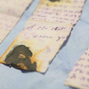Still from Number 387. A close-up shot of a torn and burned handwritten note placed on blue fabric.