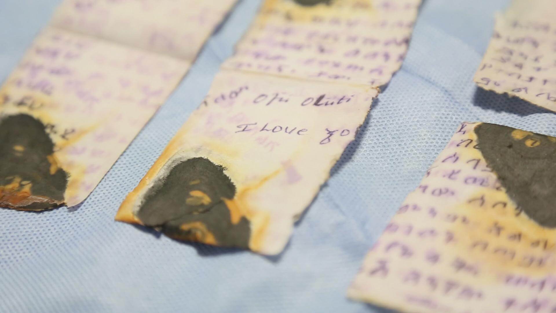Still from Number 387. A close-up shot of a torn and burned handwritten note placed on blue fabric.