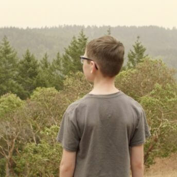 A young boy stands in front of the camera. He looks at the landscape in front of him.