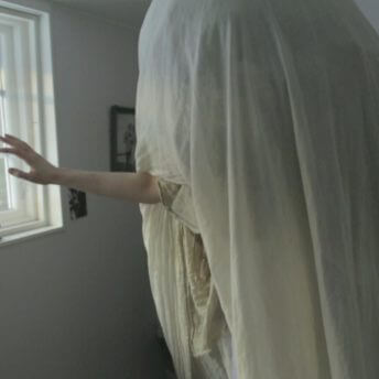 A person under a white sheet extends an arm out.