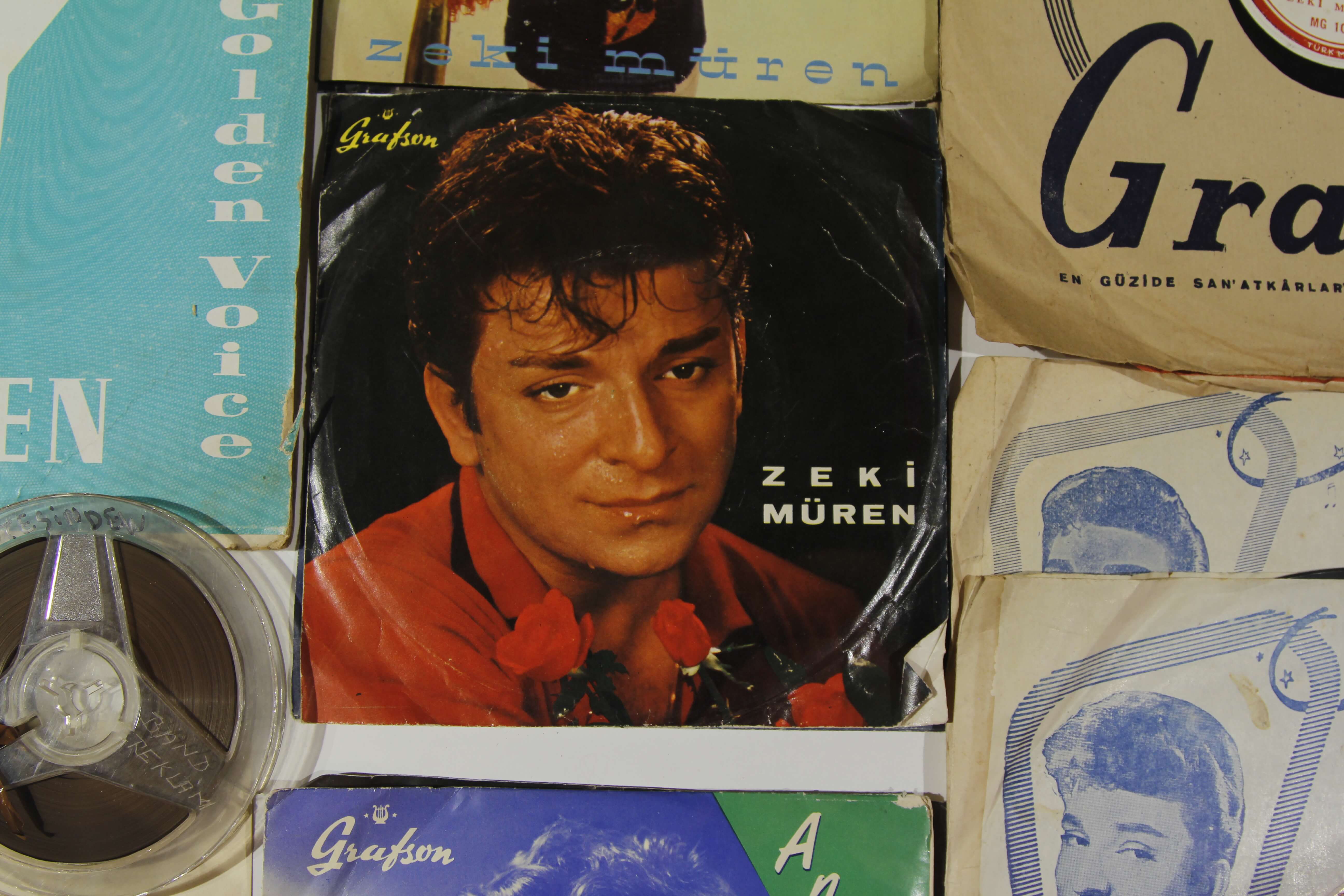 Still from A Prince from Outer Space: Zeki Muren. The record album of Zeki Muren is sitting on a table with other publications and media. On the record is an image of Zeki Muren with some red roses.