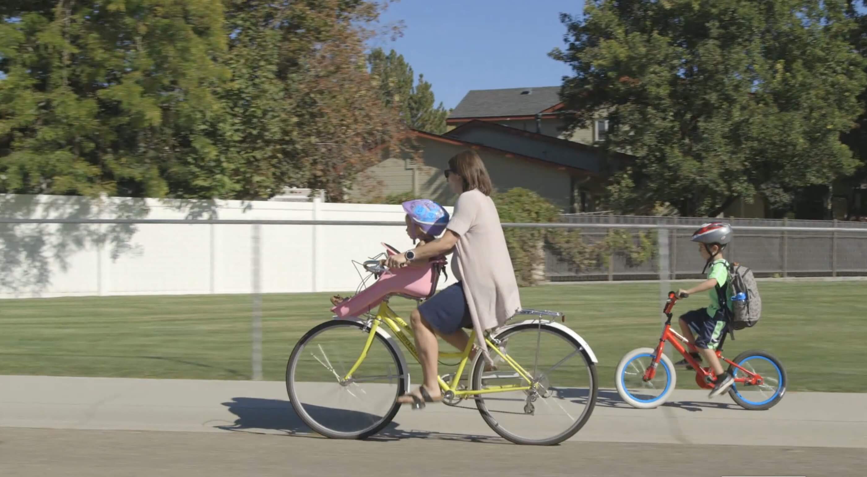 Still from Made in Boise. A woman is outside riding a bike down the sidewalk of a neighborhood street.