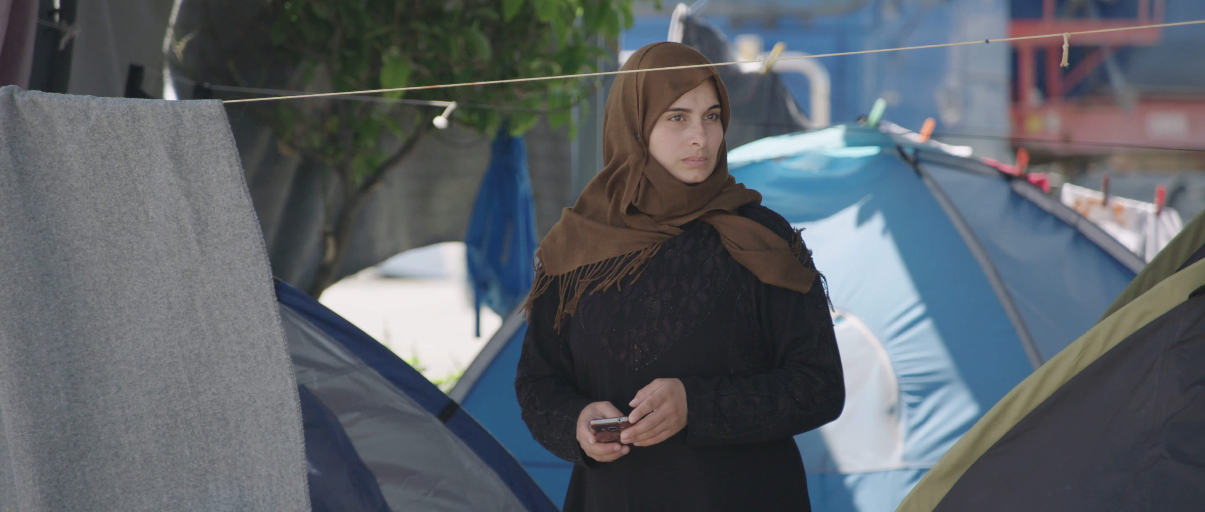 Medium shot of a young woman wearing a hijab, surrounded by camping houses.