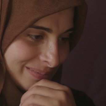 Close-up to the face of a young woman wearing a hijab, she looks away from the camera.