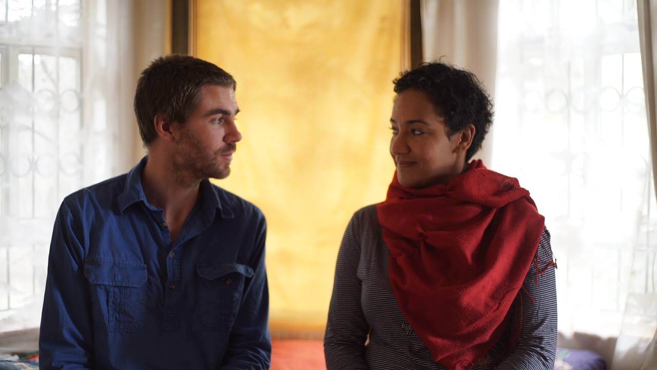 Production still from The Letter. Maia von Lekow and Chris King stand in the center of the frame, looking at each other. They both have small smiles on their face.