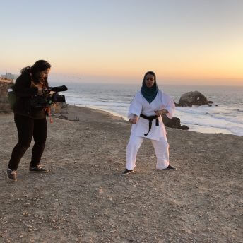Production still of An Act of Worship. A camerawoman is recording a woman practicing karate. It is the sunset.