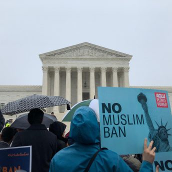 Still from An Act of Worship. People participating in a protest outside the United States Supreme Court Building. One of them is holding a poster that says "No Muslim Ban"