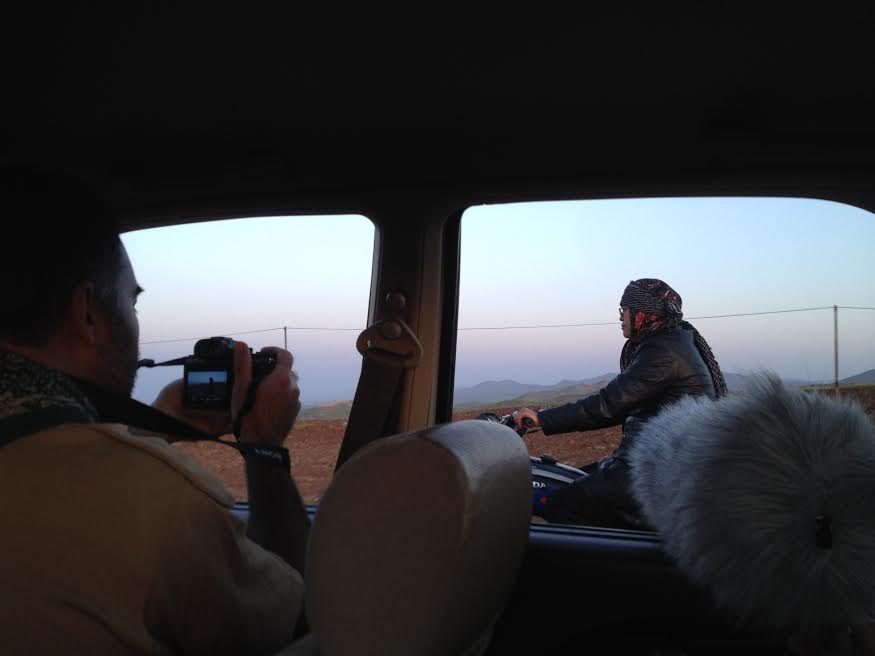 Taken from a moving car, a cameraman records a man on a motorcycle.