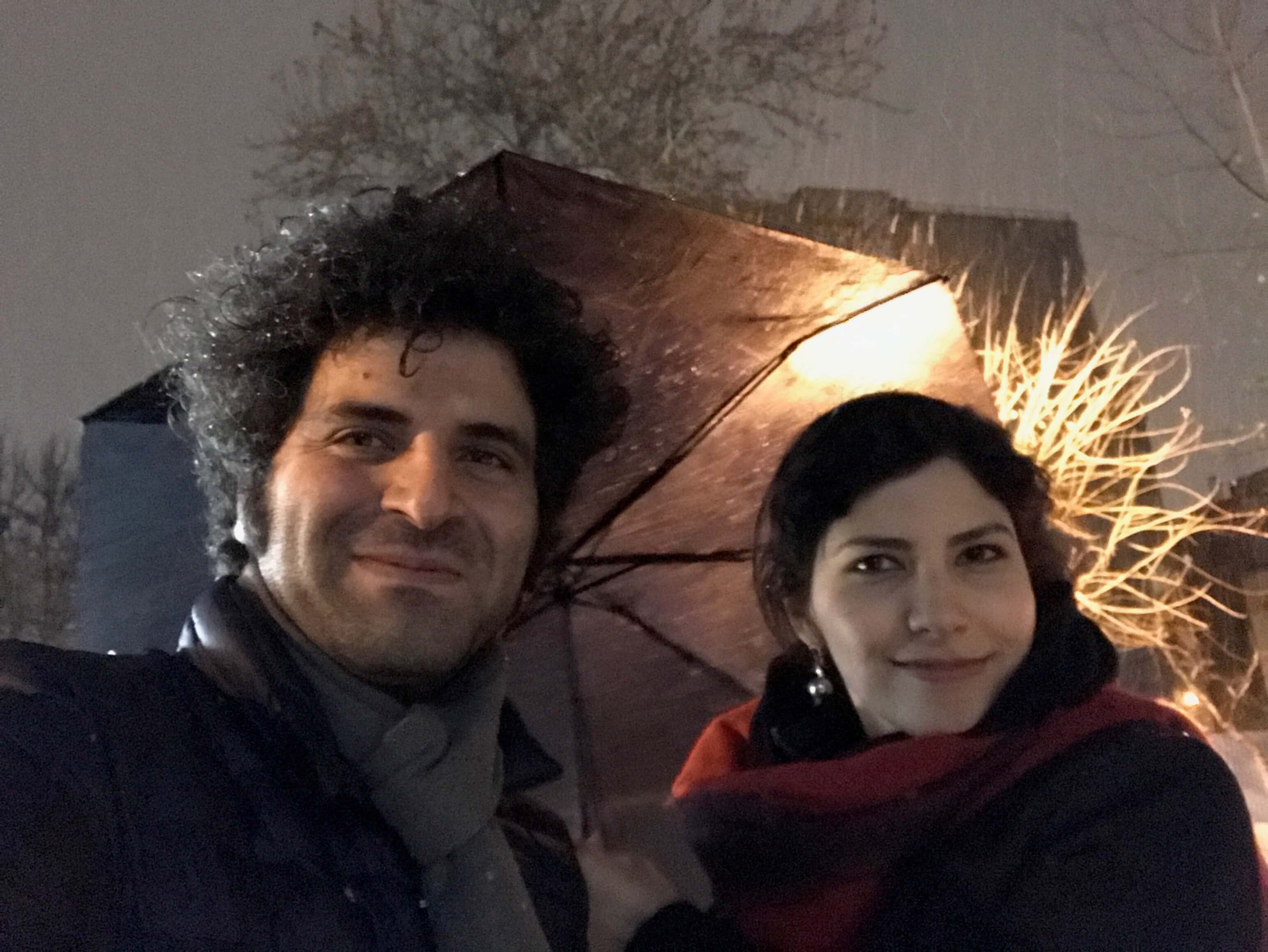 Sara Khaki and Mohammad Reza Eyni look directly at the camera and smile. It's nighttime and they wear winter clothes.