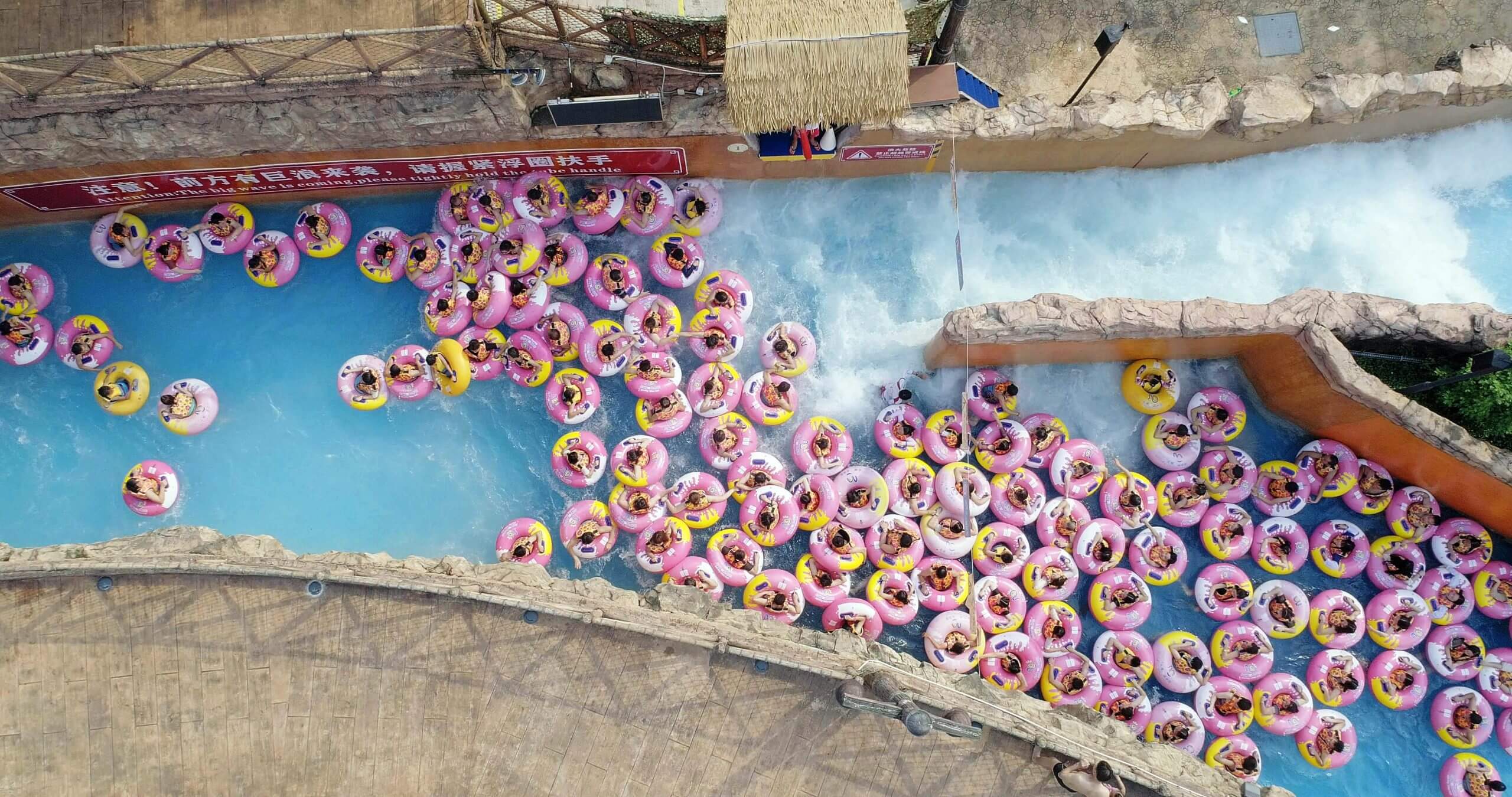 Still from Ascension. Aerial shot of a waterpark, where people are floating in circled water floats.