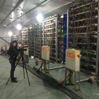 Production still from Ascension. Director Jessica Kingdon is working with a camera on a tripod in a warehouse with cables.