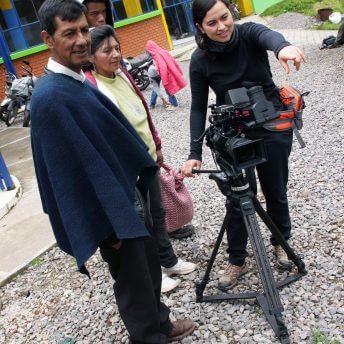 Production still of Paths of Fire. Filmmaker Viviana Gómez Echeverry is working with a camera on a tripod, pointing at something with her finger, there are two people next to her paying attention to what she is doing.