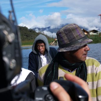 Production still of Paths of Fire. Over the shoulder shot of three men traveling on a boat, they are wearing warm clothing.
