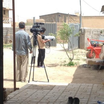A cameraman with a tripod, and Mohammad Reza working with audio equipment in a backyard.