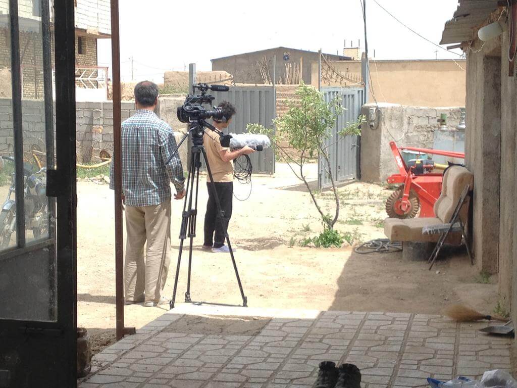 A cameraman with a tripod, and Mohammad Reza working with audio equipment in a backyard.